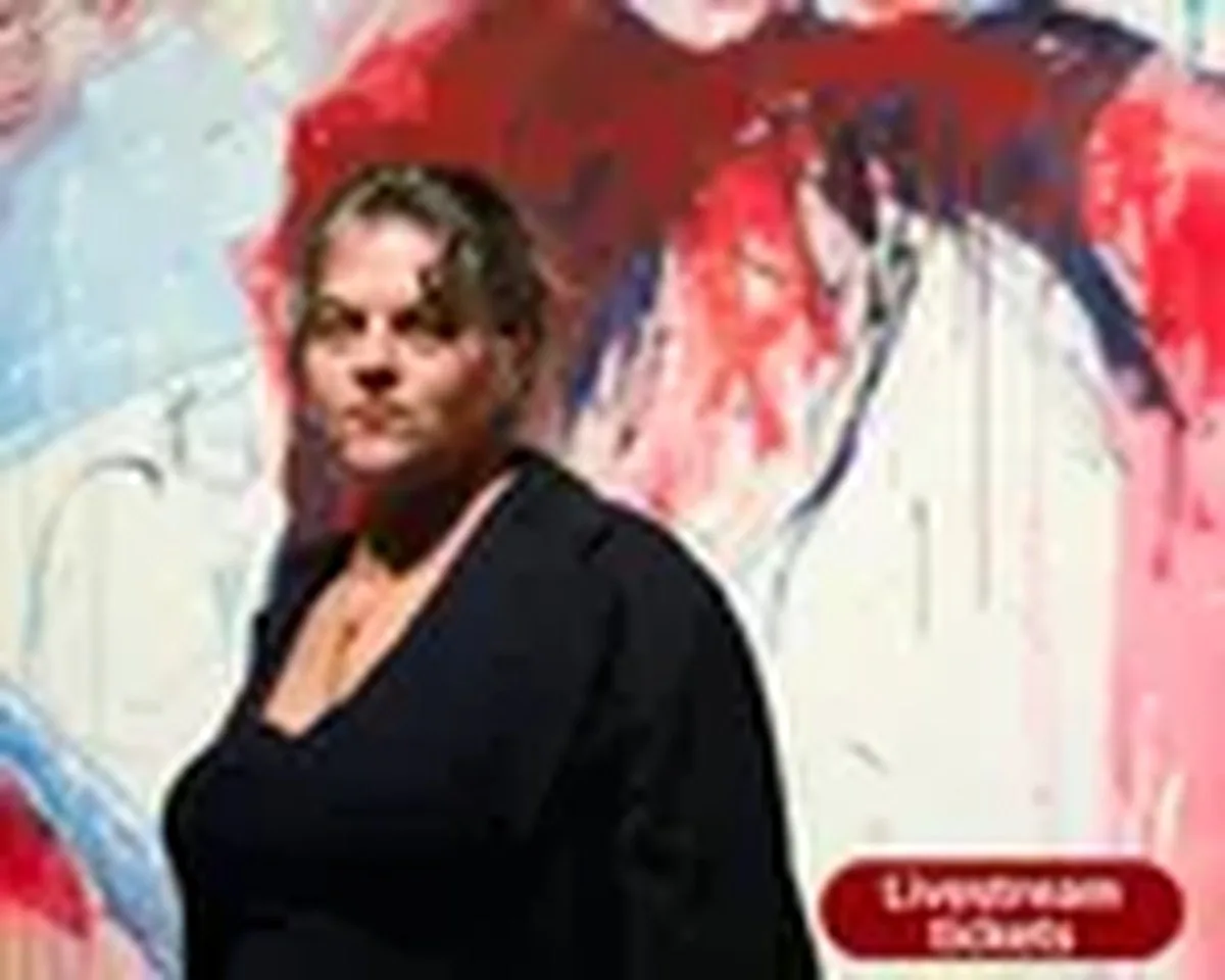 Tracey Emin stands in front of a large red, blue, and white abstract painting with bold, gestural brushstrokes and drips. She wears a black outfit and a gold necklace, facing the camera with a serious, direct expression.