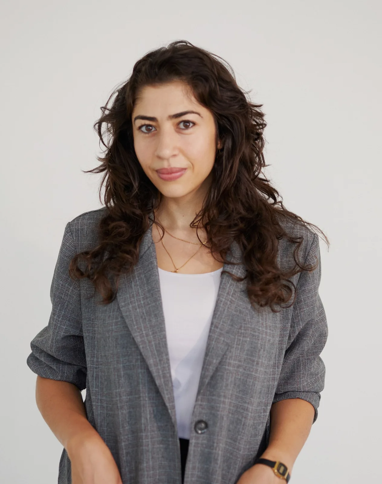 a woman wearing a grey blazer poses for the camera against a plain, grey background