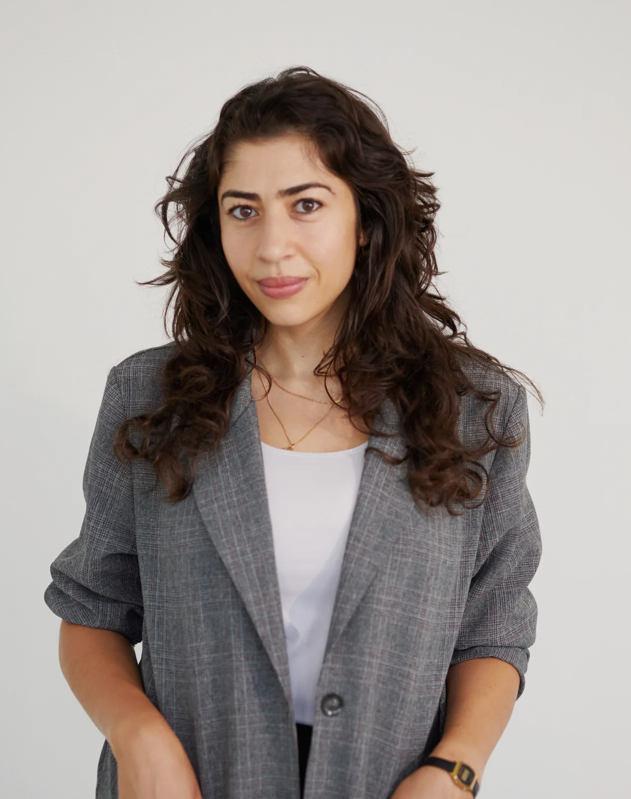 a woman wearing a grey blazer poses for the camera against a plain, grey background