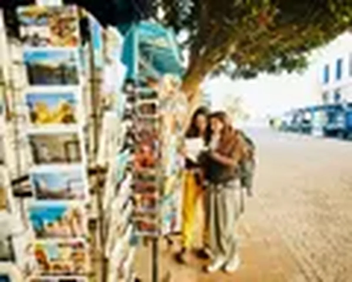 Wide shot sisters browsing through postcards at vendor in EssaouiraWide shot of smiling adult sisters browsing through postcards at street vendor while exploring Essaouira during backpacking trip in Morocco